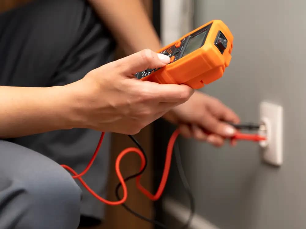 Electricista con un multímetro naranja midiendo la tensión de un tomacorriente en la pared