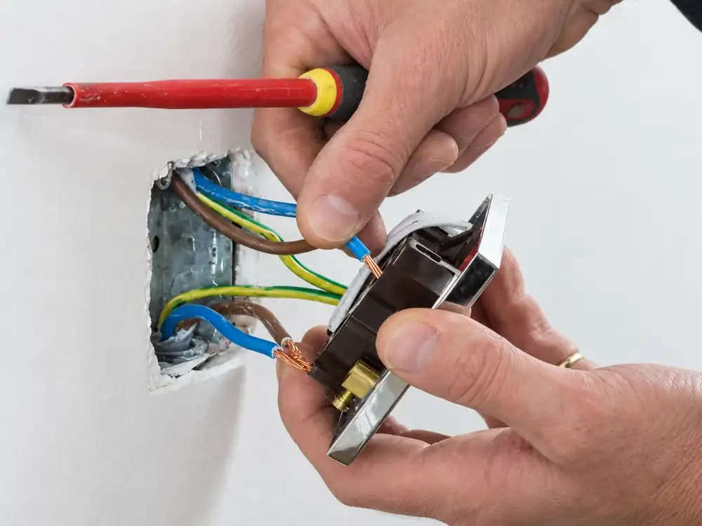 Manos conectando los cables de un tomacorriente empotrado en la pared con un destornillador aislado