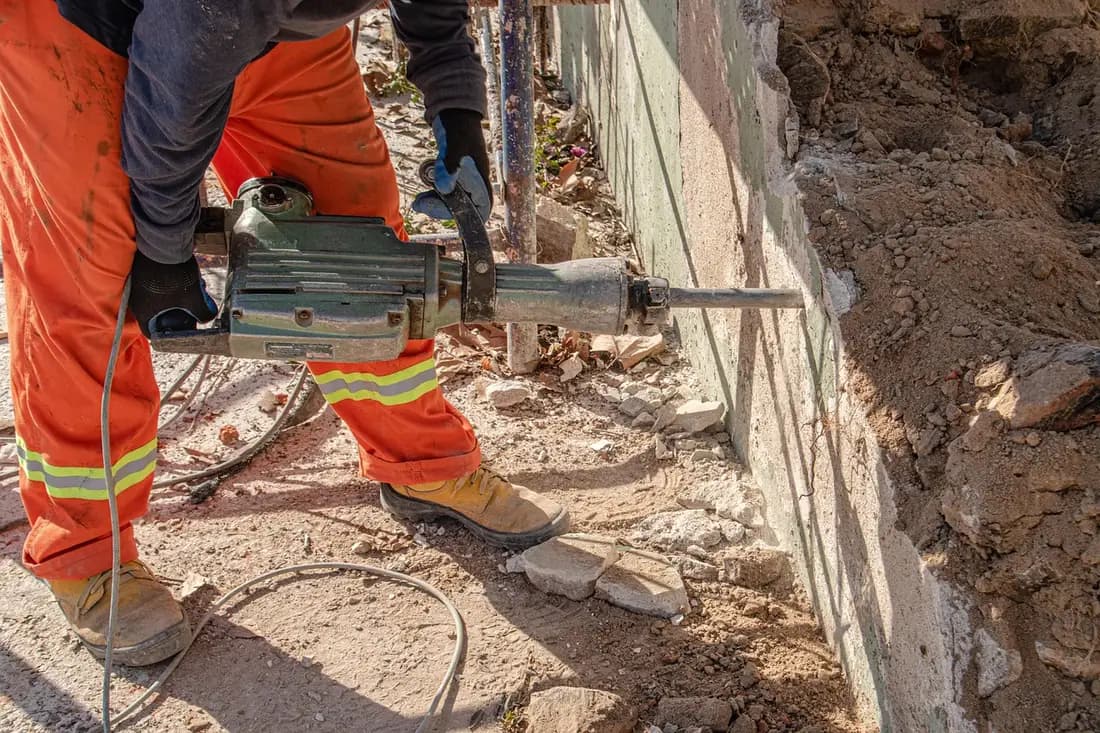Obrero con martillo demoledor rompiendo un muro de concreto