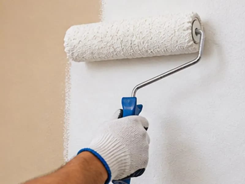 Mano con guante pintando una pared con rodillo