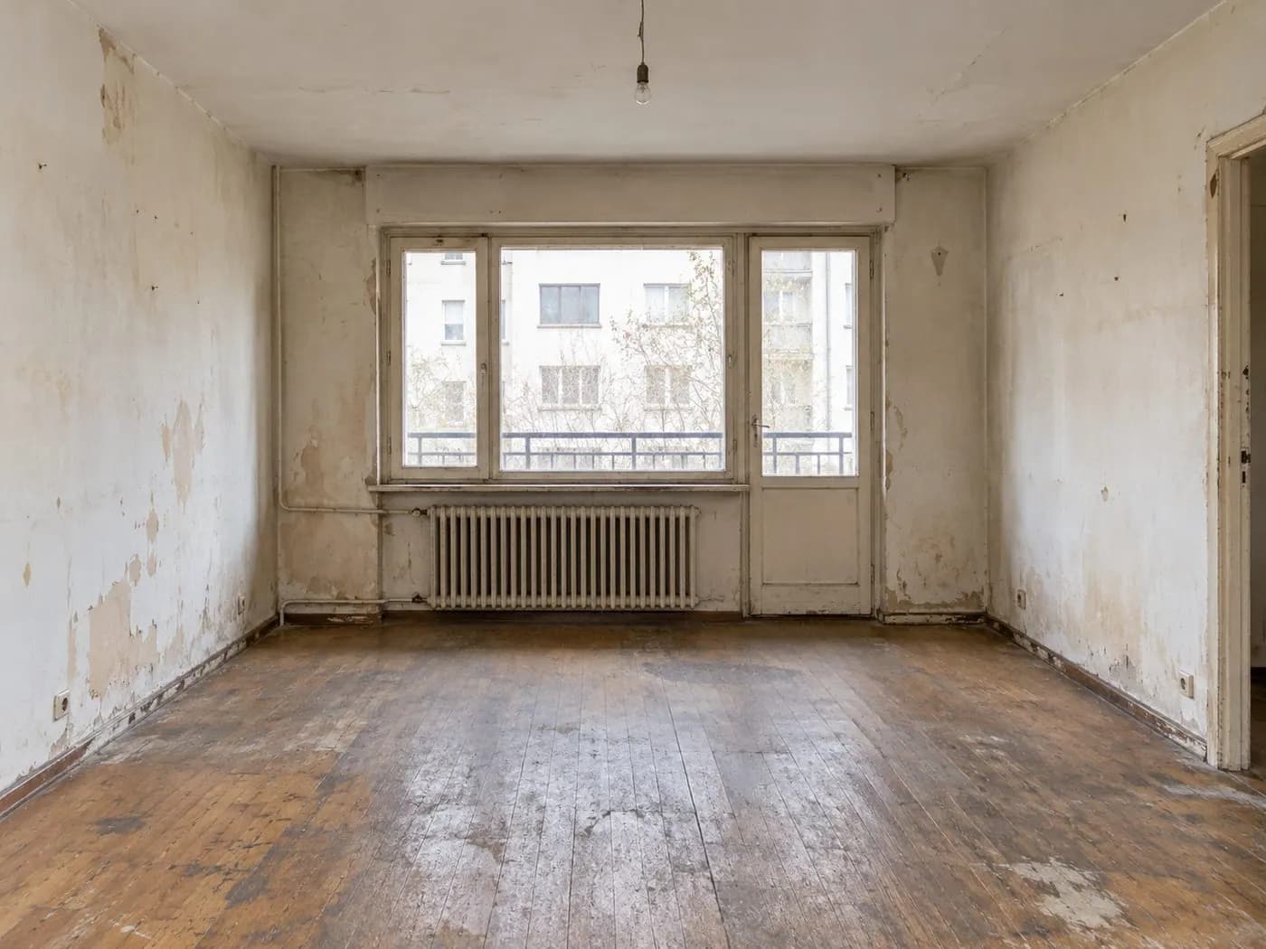 Sala antes de renovar: paredes con humedad y pintura desprendida, piso de madera deteriorado